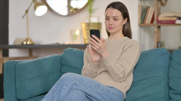 Jovem mulher usando smartphone no sofá — Fotografia de Stock