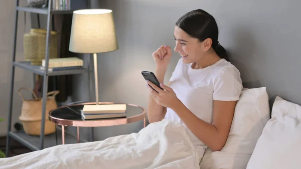 Успіх, латинська жінка святкує на Смартфоні в ліжку — стокове фото