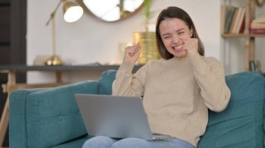 Dizüstü bilgisayarlı başarılı genç kadın koltukta kutlama yapıyor. 