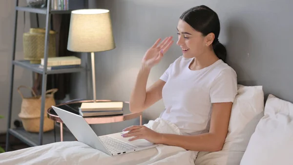 Czat wideo na laptopie przez młoda Latynoska kobieta w łóżku — Zdjęcie stockowe