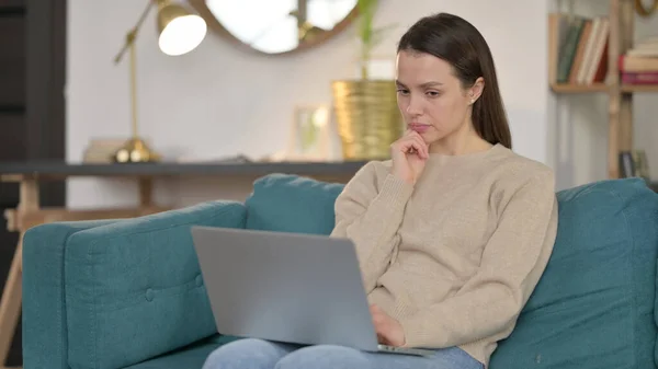 Junge Frau mit Laptop denkt auf Sofa — Stockfoto
