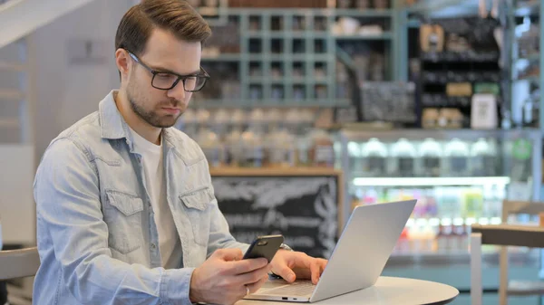 Homme créatif avec ordinateur portable en utilisant Smartphone dans Cafe — Photo