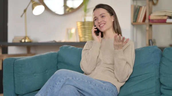 Junge Frau spricht auf dem Sofa mit Smartphone — Stockfoto