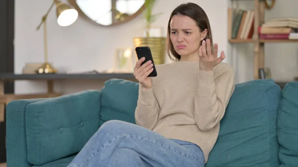 Junge Frau reagiert auf Verlust mit Smartphone auf Sofa — Stockfoto