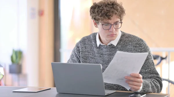 Junger Mann mit Dokumenten am Laptop — Stockfoto