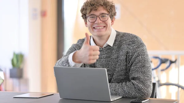 Pozytywny młody człowiek z laptopem pokazując kciuki w górę — Zdjęcie stockowe
