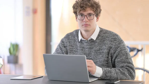 Jeune homme avec ordinateur portable regardant la caméra — Photo