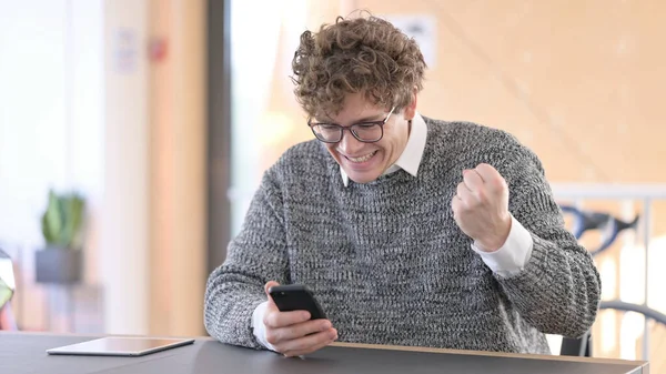 Jeune homme acclamant sur Smartphone au travail, Succès — Photo