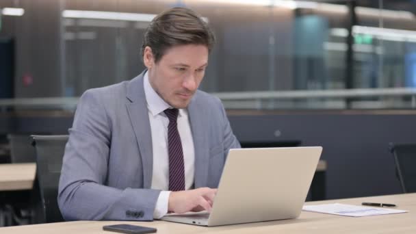Бизнесмен среднего возраста с ноутбуком, указывающий на камеру — стоковое видео