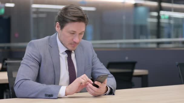 Бізнесмен середнього віку користується смартфоном в офісі — стокове відео