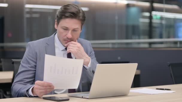 Empresario de mediana edad leyendo documentos mientras usa el ordenador portátil — Vídeos de Stock