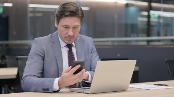 노트북을 가진 중년의 사업가 사무실에서 스마트 폰을 사용하는 모습 — 비디오