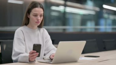 Laptop üzerinde çalışırken Smartphone kullanan kadın