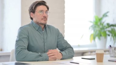 Orta yaşlı bir adam ofiste oturmuş düşünüyor. 