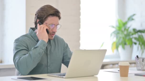 Hombre enojado con el ordenador portátil hablando en el teléfono inteligente — Vídeo de stock