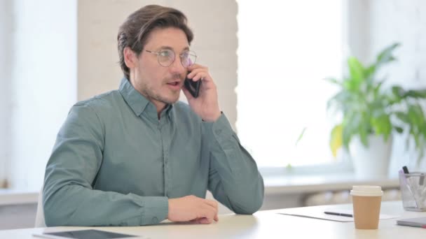 Среднего возраста человек разговаривает на смартфоне в офисе — стоковое видео