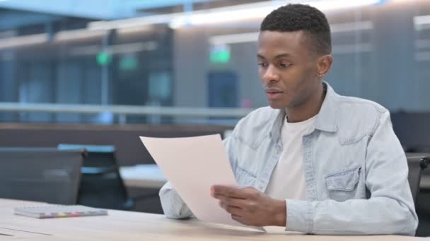 Uomo africano che reagisce alla perdita durante la lettura di documenti — Video Stock