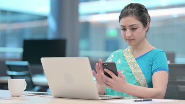Ινδική γυναίκα με φορητό υπολογιστή χρησιμοποιώντας Smartphone στο χώρο εργασίας — Αρχείο Βίντεο