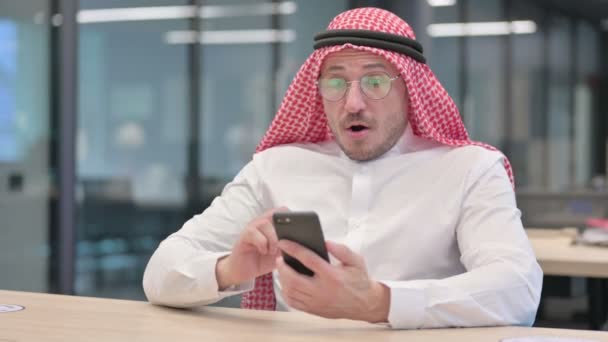 Арабский мужчина среднего возраста реагирует на потери на смартфоне в офисе — стоковое видео