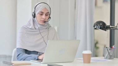 Kulaklıklı genç Arap kadın dizüstü bilgisayarda çalışıyor.