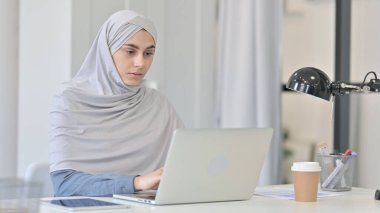 Ofiste dizüstü bilgisayarda çalışan genç bir Arap kadın. 