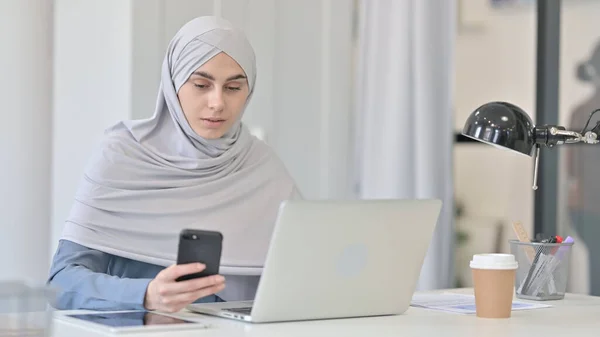 办公室使用智能手机的阿拉伯青年妇女与笔记本电脑 — 图库照片