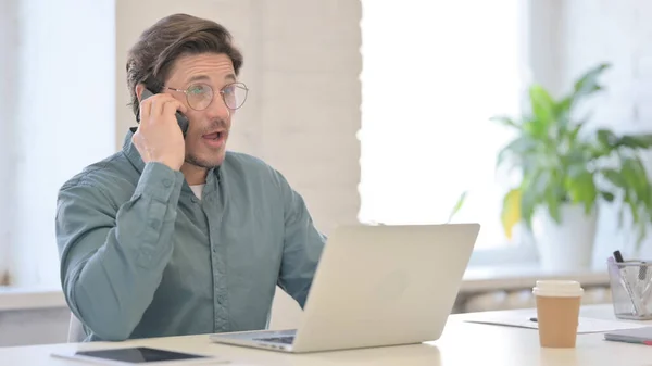 Hombre de mediana edad con el ordenador portátil hablando en el teléfono inteligente — Foto de Stock