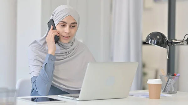 Молода арабська жінка з ноутбуком розмовляє на смартфоні — стокове фото