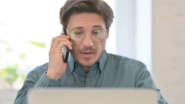 Retrato del hombre de mediana edad con el ordenador portátil hablando en el teléfono inteligente —  Fotos de Stock