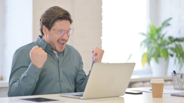 Exitoso hombre de mediana edad celebrando en el ordenador portátil en la oficina —  Fotos de Stock