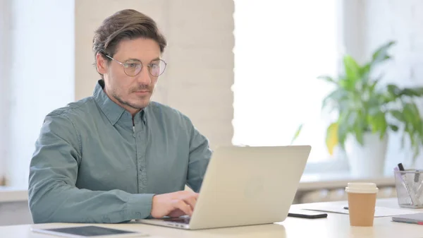 Hombre de mediana edad que trabaja en el ordenador portátil en la oficina — Foto de Stock