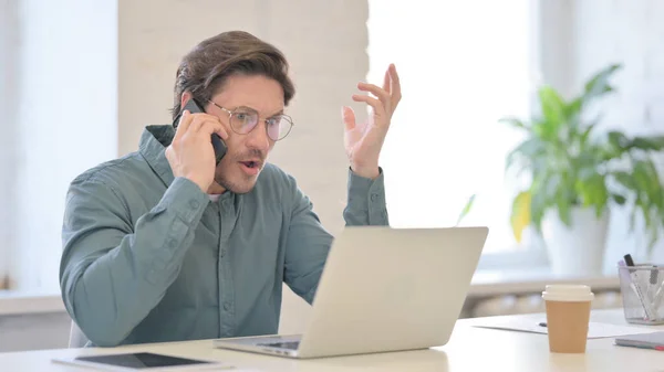 怒っている男とノートパソコンで話すスマートフォン — ストック写真