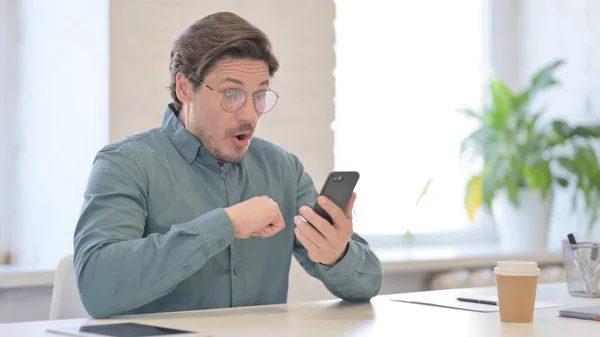 Middelbare leeftijd Man reageert op verlies op Smartphone in Office — Stockfoto