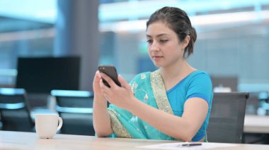 İş yerinde akıllı telefon kullanan genç Hintli kadın.