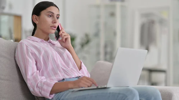 Latynoska kobieta z laptopem rozmawia na smartfonie w domu — Zdjęcie stockowe