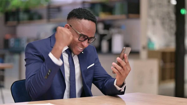 Junger afrikanischer Geschäftsmann feiert Erfolg mit Smartphone im Büro — Stockfoto