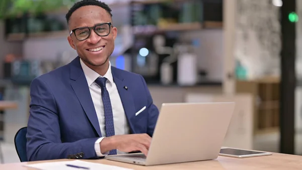 Ung afrikansk affärsman med bärbar dator ler mot kameran i Office — Stockfoto