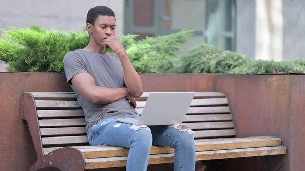 非洲年轻人在长椅上思考和使用笔记本电脑 — 图库照片