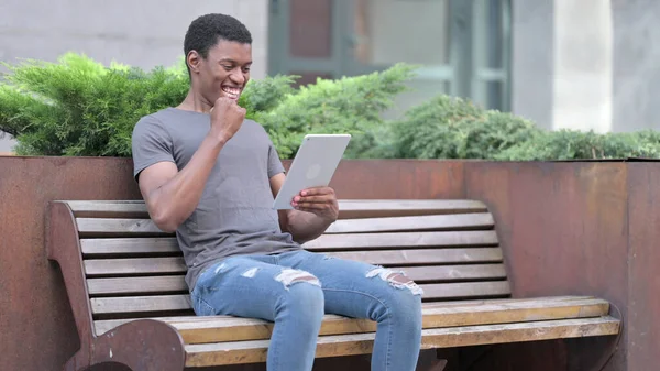Mladý Afričan slaví úspěch na tabletu na lavičce — Stock fotografie