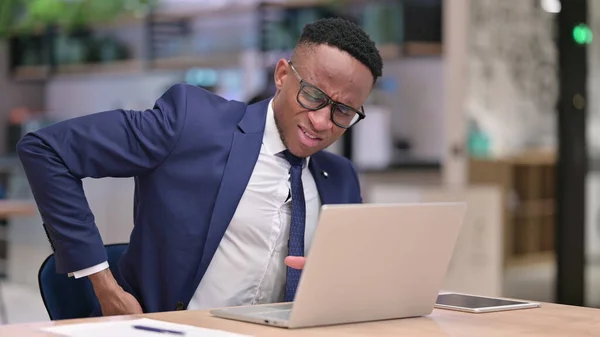 Hårt arbetande ung afrikansk affärsman med bärbar dator som har ryggvärk i kontoret — Stockfoto