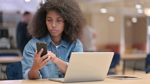 Afrikanerin nutzt Smartphone und Laptop bei der Arbeit — Stockfoto