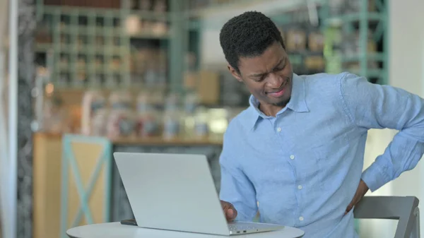 Junger Afrikaner mit Rückenschmerzen benutzt Laptop im Café — Stockfoto