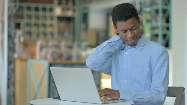 Jeune homme africain avec ordinateur portable ayant la douleur au cou dans le café — Photo