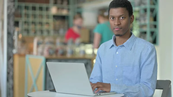 Allvarlig afrikansk man med bärbar dator tittar på kameran i Café — Stockfoto