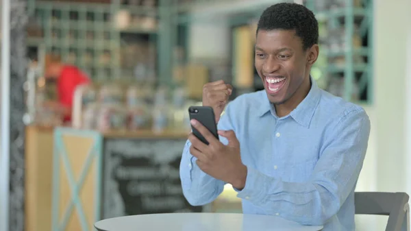 Ambiciózus fiatal afrikai férfi ünnepli siker az intelligens telefon — Stock Fotó