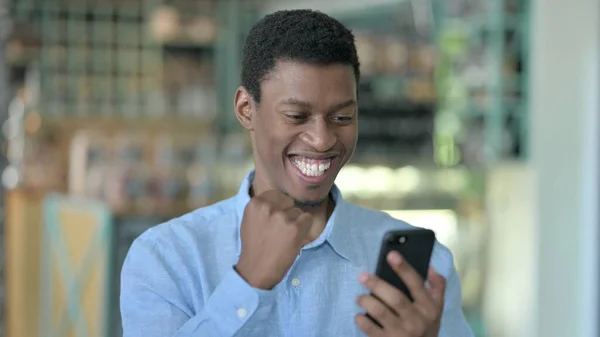 Porträt eines aufgeregten jungen Afrikaners, der auf dem Smartphone feiert — Stockfoto