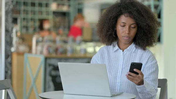 Jeune femme africaine en utilisant Smartphone et ordinateur portable à Cafe — Photo