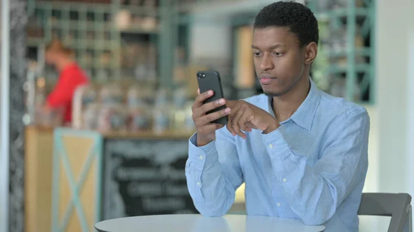 Junger Afrikaner benutzt Smartphone im Café — Stockfoto