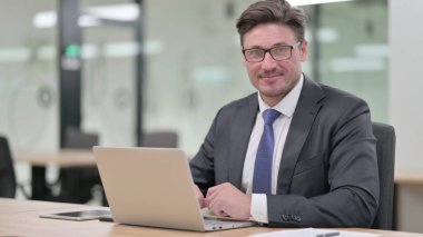 Orta yaşlı iş adamı dizüstü bilgisayarla evet işareti gösteriyor.