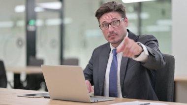 Bilgisayarlı orta yaşlı iş adamı kamerayı işaret ediyor. 